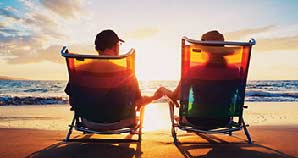 Retired couple sitting on beach watching the sunset.